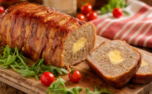 Un cake salé au Babybel enroulé de tranches de bacon croustillantes sur une planche en bois.