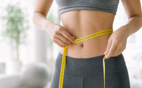 Une femme mesurant son tour de taille avec un ruban jaune dans une salle de sport.
