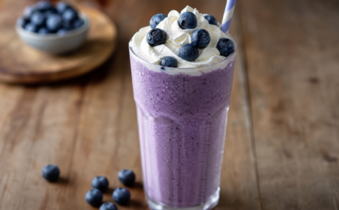Un verre de milkshake à la myrtille avec crème fouettée sur une table en bois.