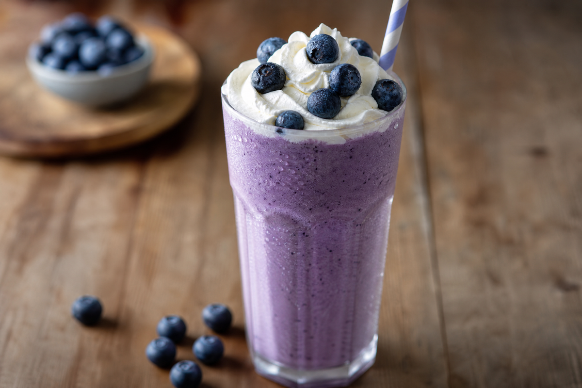 Un verre de milkshake à la myrtille avec crème fouettée sur une table en bois.