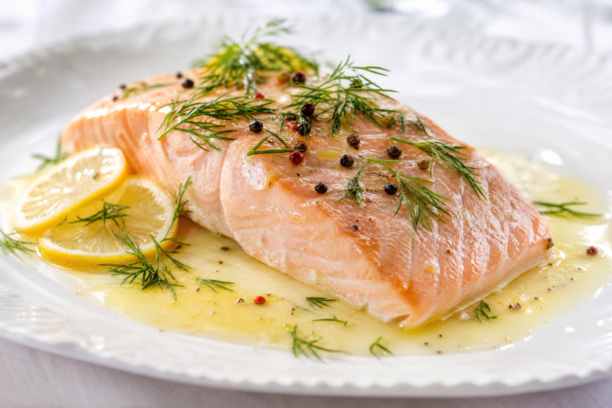 Pavé de saumon poché à la sauce beurre blanc, citron et aneth sur une assiette. 
