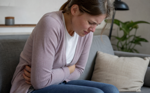 Une femme se tenant le ventre de douleur sur son canapé.
