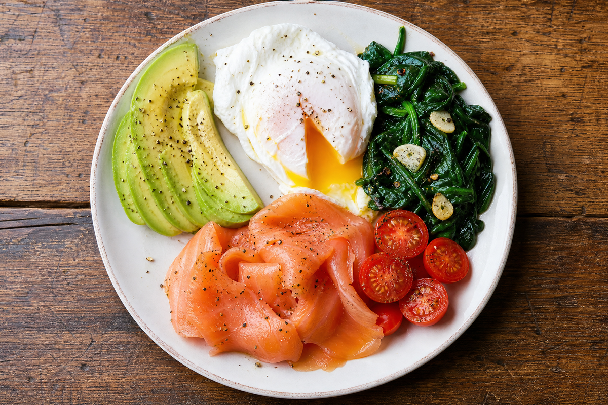 Assiette de petit-déjeuner équilibré avec œuf poché, saumon fumé, avocat, épinards et tomates cerises.