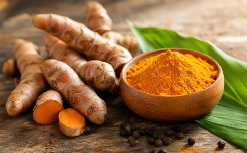 Racines de curcuma frais et curcuma en poudre dans un bol en bois sur une table.