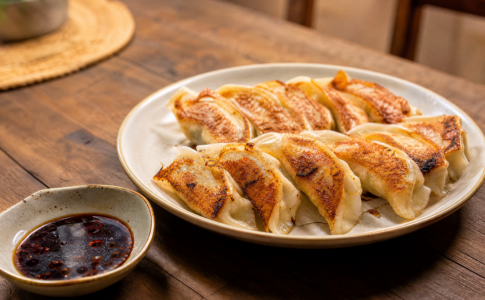 Assiette de gyozas japonais dorés et poêlés servis avec une coupelle de sauce soja.