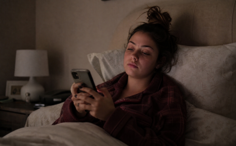 Jeune femme allongée dans son lit fixant son smartphone avec un air ennuyé.