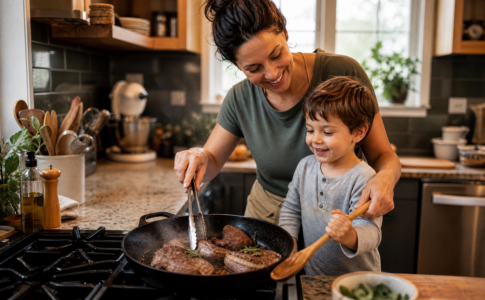 Mère et son fils cuisinant des morceaux de viande dans une poêle à la maison.