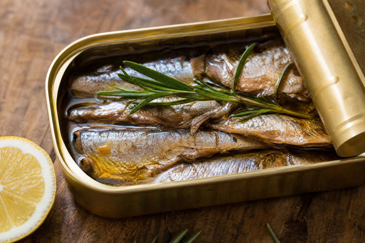 Boîte de conserve ouverte contenant des sardines à l'huile avec du romarin et du citron.