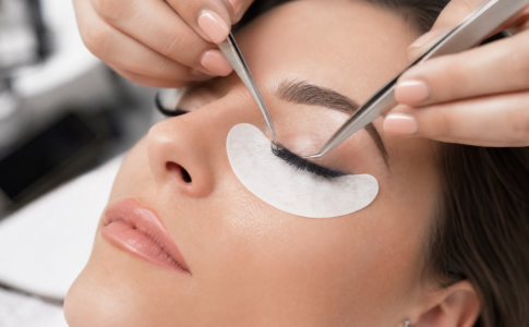 Esthéticienne appliquant délicatement des extensions de cils à l’aide de deux pinces sur une cliente.