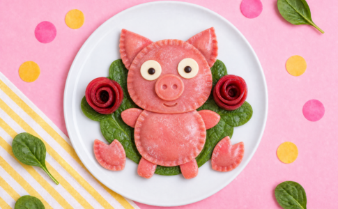 Des raviolis roses en forme de petits cochons servis avec des épinards.
