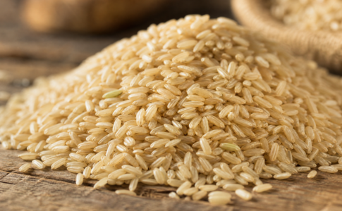 Des grains de riz brun entier présentés sur une surface en bois rustique.