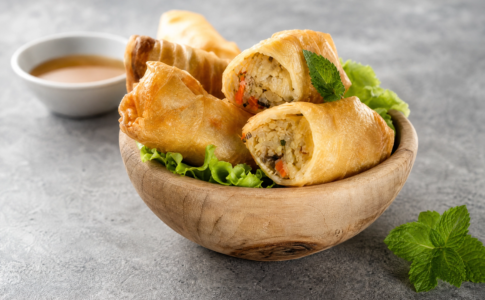Rouleaux de printemps frais garnis de légumes et de crevettes, accompagnés d'une sauce.